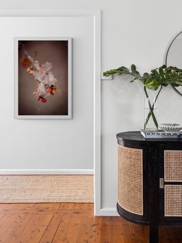 Minimalistyczna scena botaniczna: blady, szkieletowy płatek zaplątany w pomarańczowe jagody - druk artystyczny celebrujący poezję nieoczekiwanego.