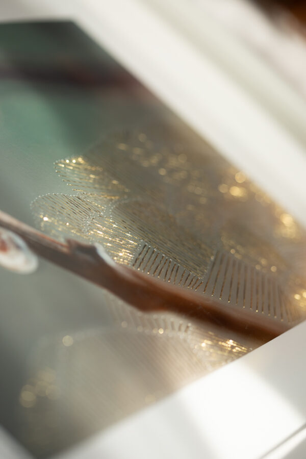 Zbliżenie detalu haftu złotą metaliczną nicią naniesionego na archiwalny wydruk pigmentowy, odsłaniający strukturę i rytm światła.